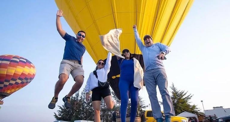 Grupo de cinco personas sosteniendo un gran globo aerostático amarillo mientras saltan al aire libre durante el día