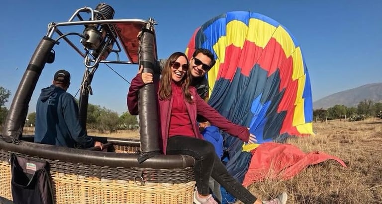 Personas en la canastilla del globo aerostático con paracaídas de inflado colorido azul, rojo y amarillo en paisaje rural