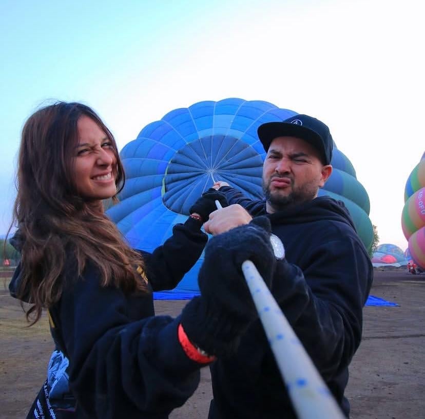 Dos personas sosteniendo una cuerda conectada a un gran globo aerostático azul durante la inflación en el sitio de lanzamiento