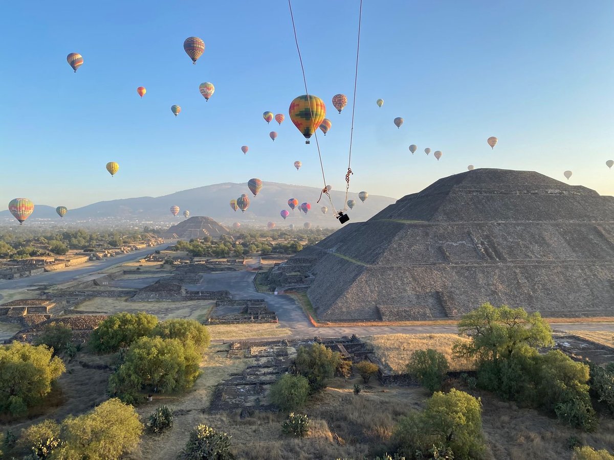 Múltiples globos aerostáticos coloridos flotando sobre una pirámide antigua y sitio arqueológico con montañas en la distancia