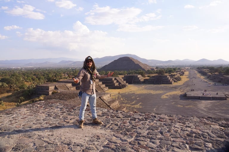 Woman standing on top of a pyramid overlooking ancient Mesoamerican ruins with mountains in the distance