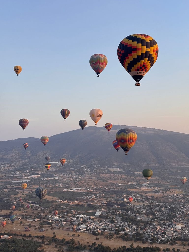 Múltiples globos aerostáticos coloridos flotando sobre un paisaje de montañas durante el amanecer o atardecer